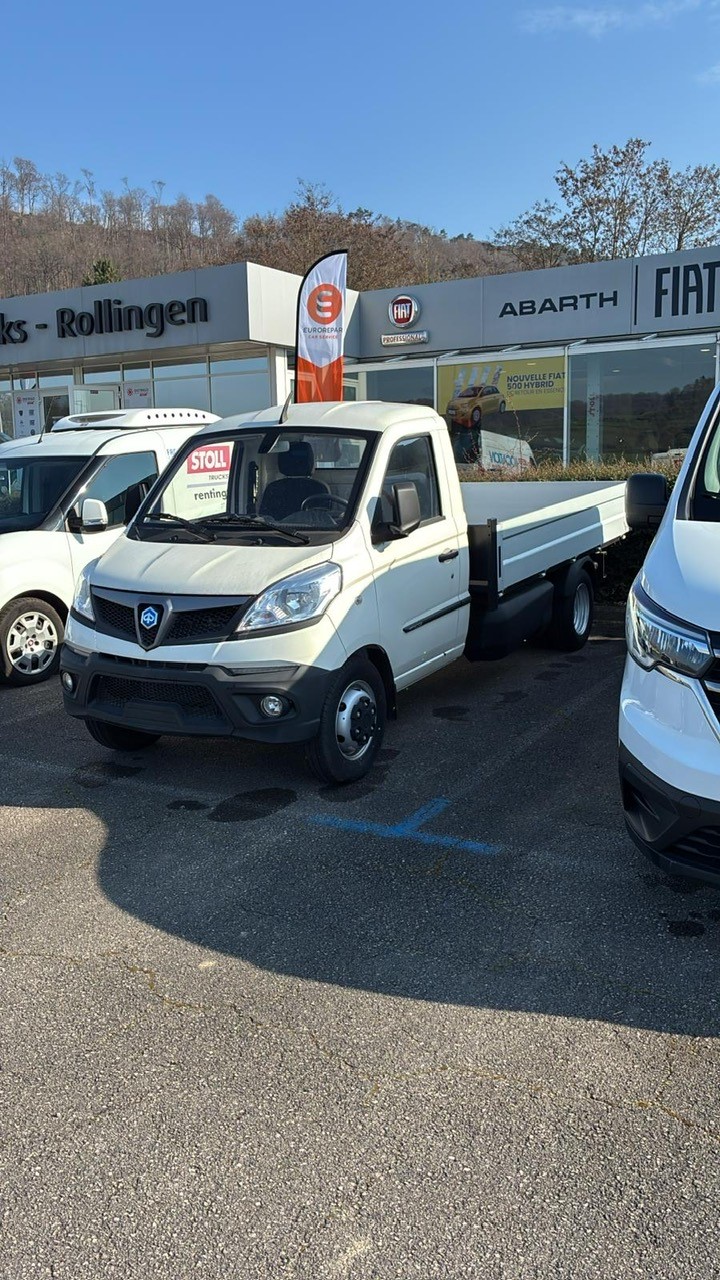 Camion blanc garé devant concession automobile.