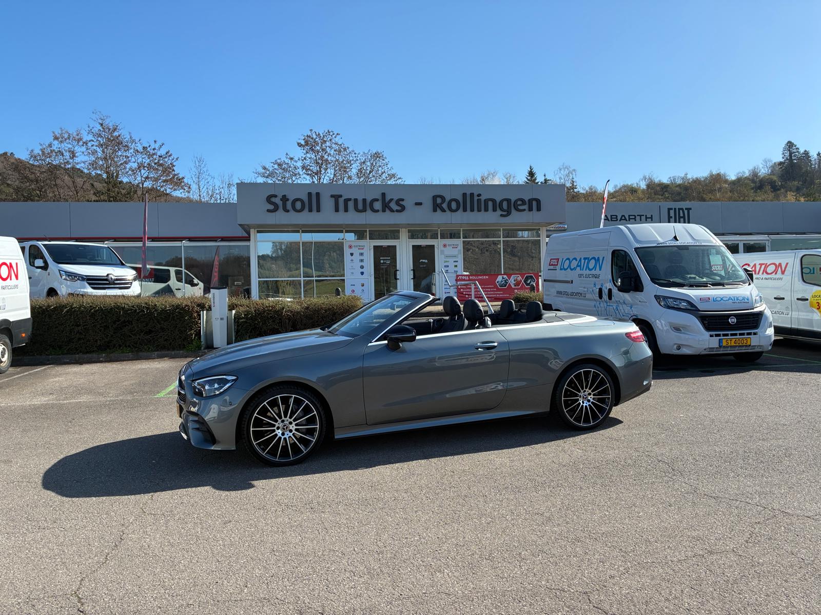 Voiture décapotable grise devant un concessionnaire.