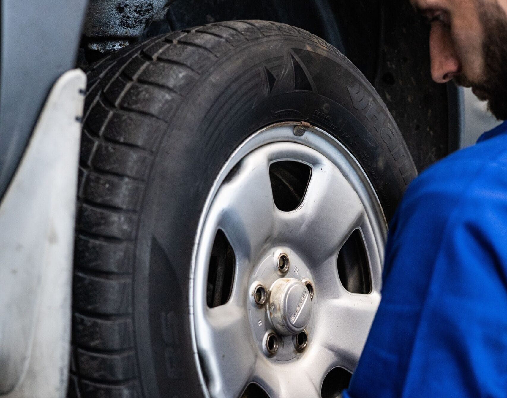 Mécanicien en bleu inspectant un pneu de voiture