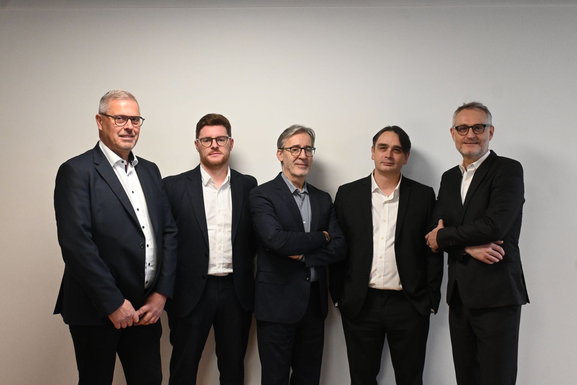 Cinq hommes en costume posent devant un mur blanc