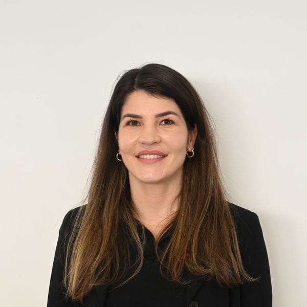 Femme souriante en veste noire devant un mur blanc