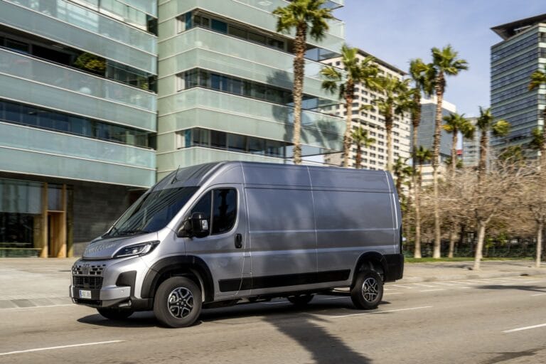 Utilitaire Fiat Ducato gris métallisé sur une route en ville avec un immeuble en arrière-plan et des palmiers.