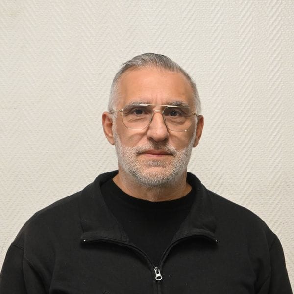 Homme avec lunettes et pull noir devant mur clair