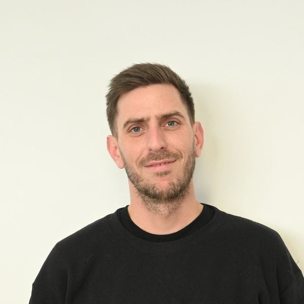 Homme souriant en pull noir devant mur clair