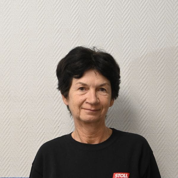 Femme souriante en pull noir devant mur clair