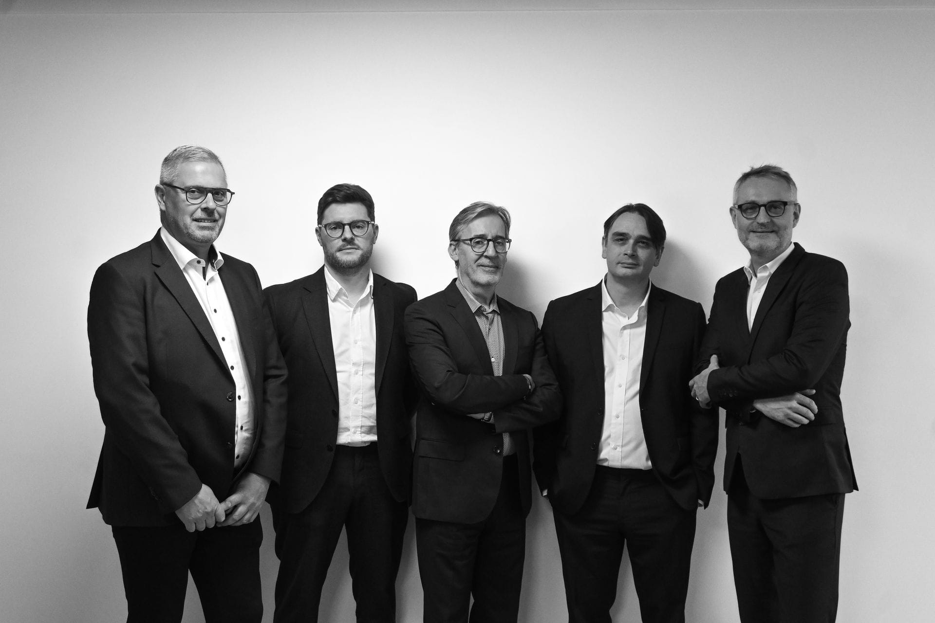 Cinq hommes en costume posent devant un mur blanc